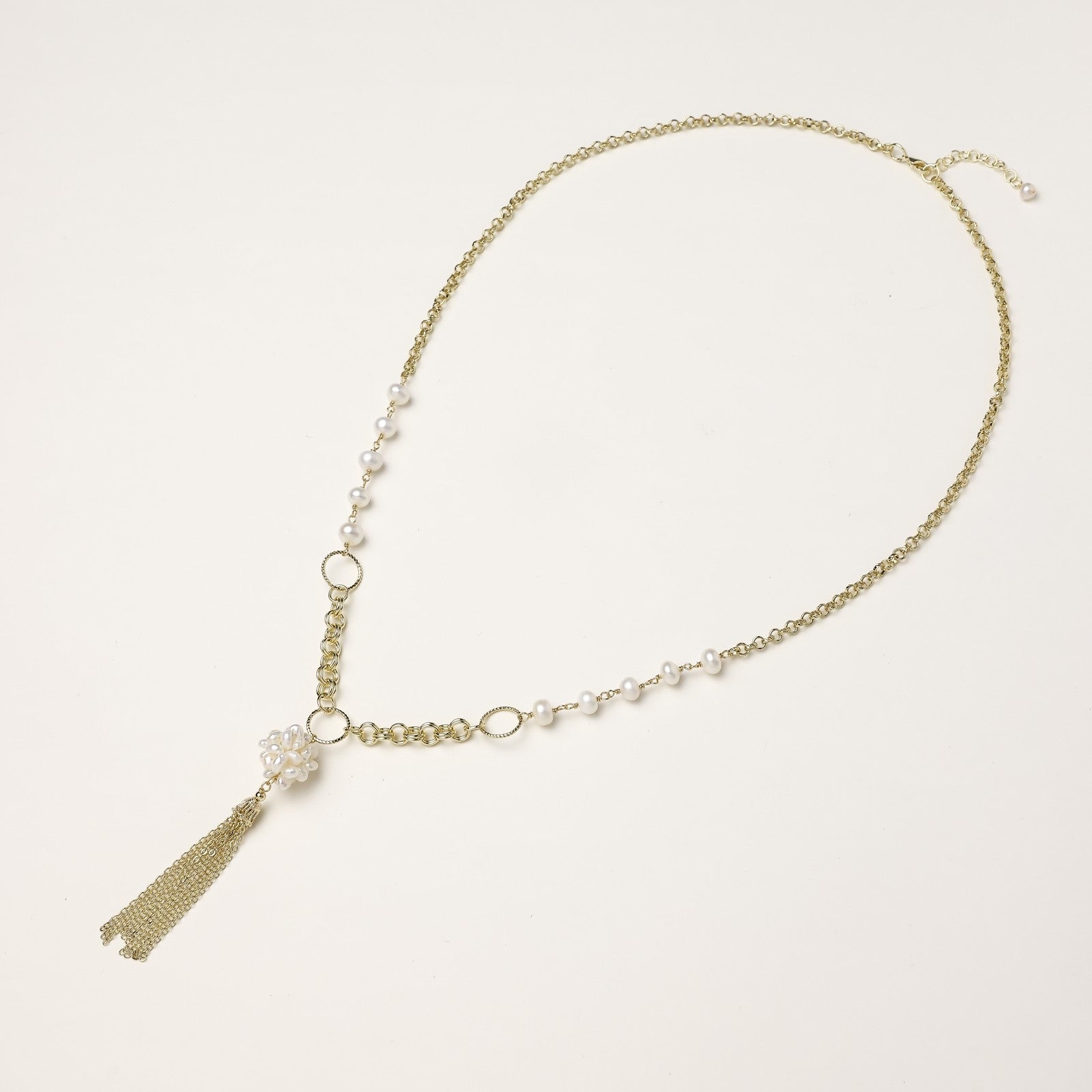 Layered gold-plated necklace with freshwater pearls, central pearl cluster, and chain tassel on cream background.
