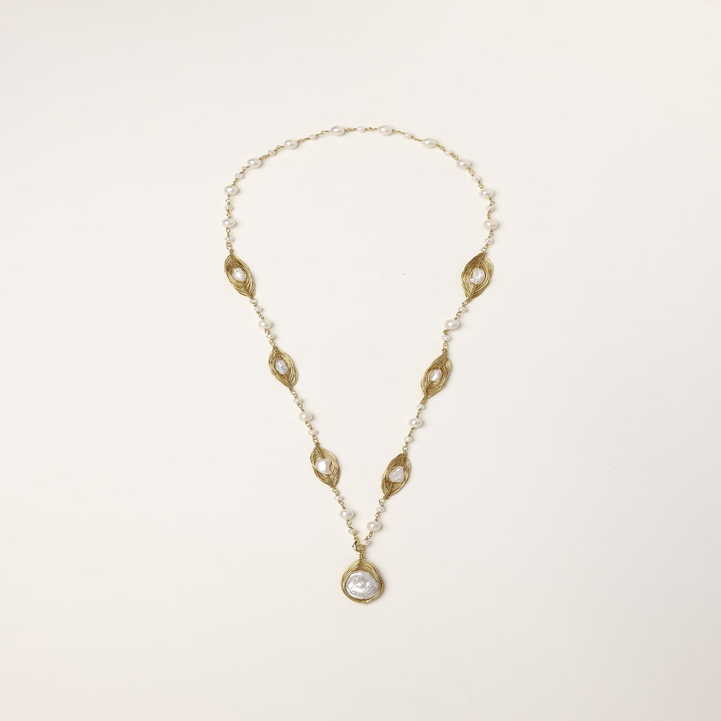 Long gold-plated necklace with eye-shaped elements, freshwater pearls, and baroque pearl pendant on neutral background.