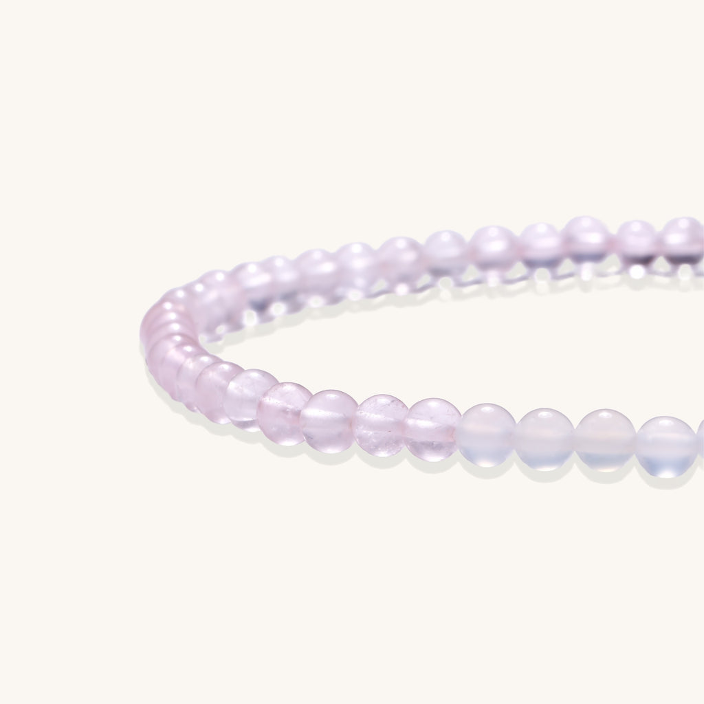 Stretchable bracelet with pink rose quartz and white agate beads, featuring a decorative tassel pendant on white background.