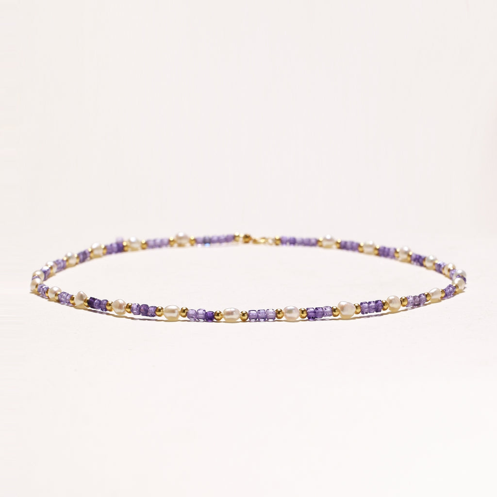 Delicate beaded necklace with alternating purple zirconia stones, white freshwater pearls, and gold-plated spacers on cream background.