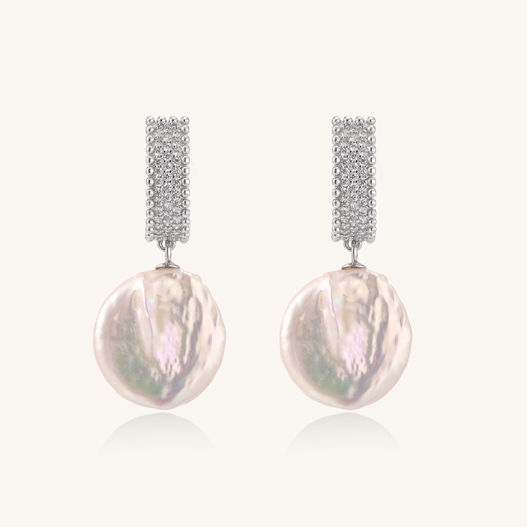 Sterling silver huggie earrings with lustrous baroque pearls displaying iridescent pink and cream tones on white background.