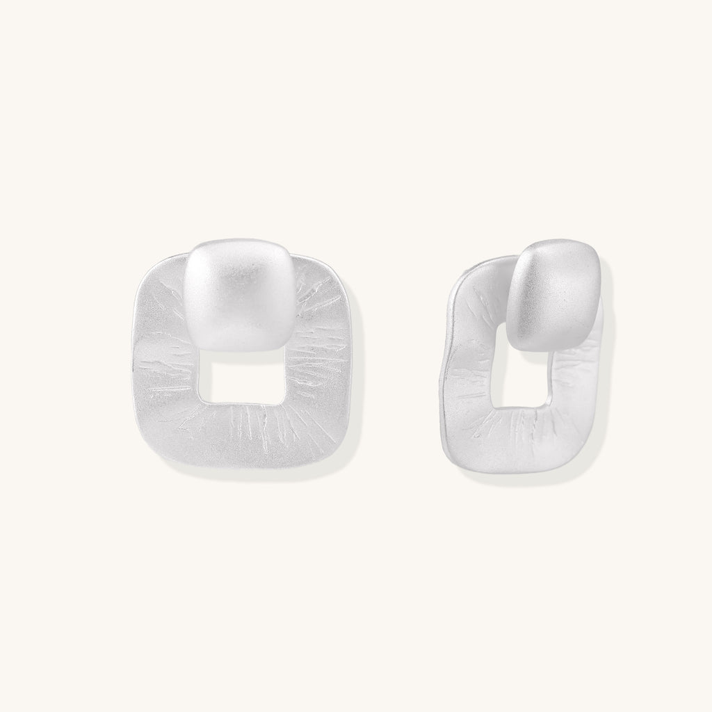 Geometric sterling silver square stud earrings with brushed texture and central square cutouts on white background.