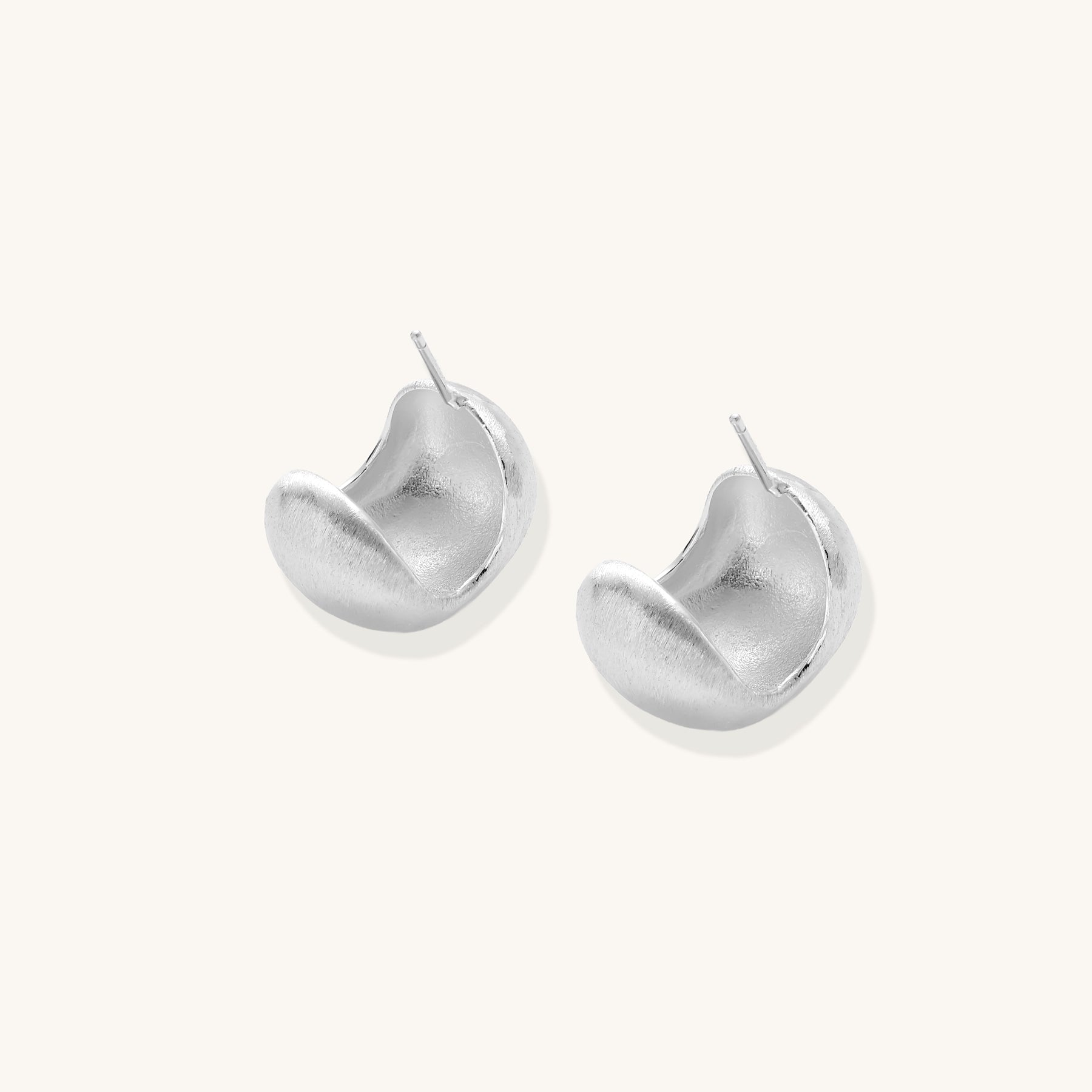 Close-up of chunky sterling silver huggie hoops with brushed matte finish against cream background.