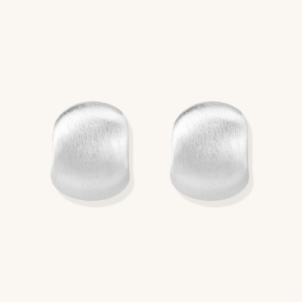 Close-up of chunky sterling silver huggie hoops with brushed matte finish against cream background.