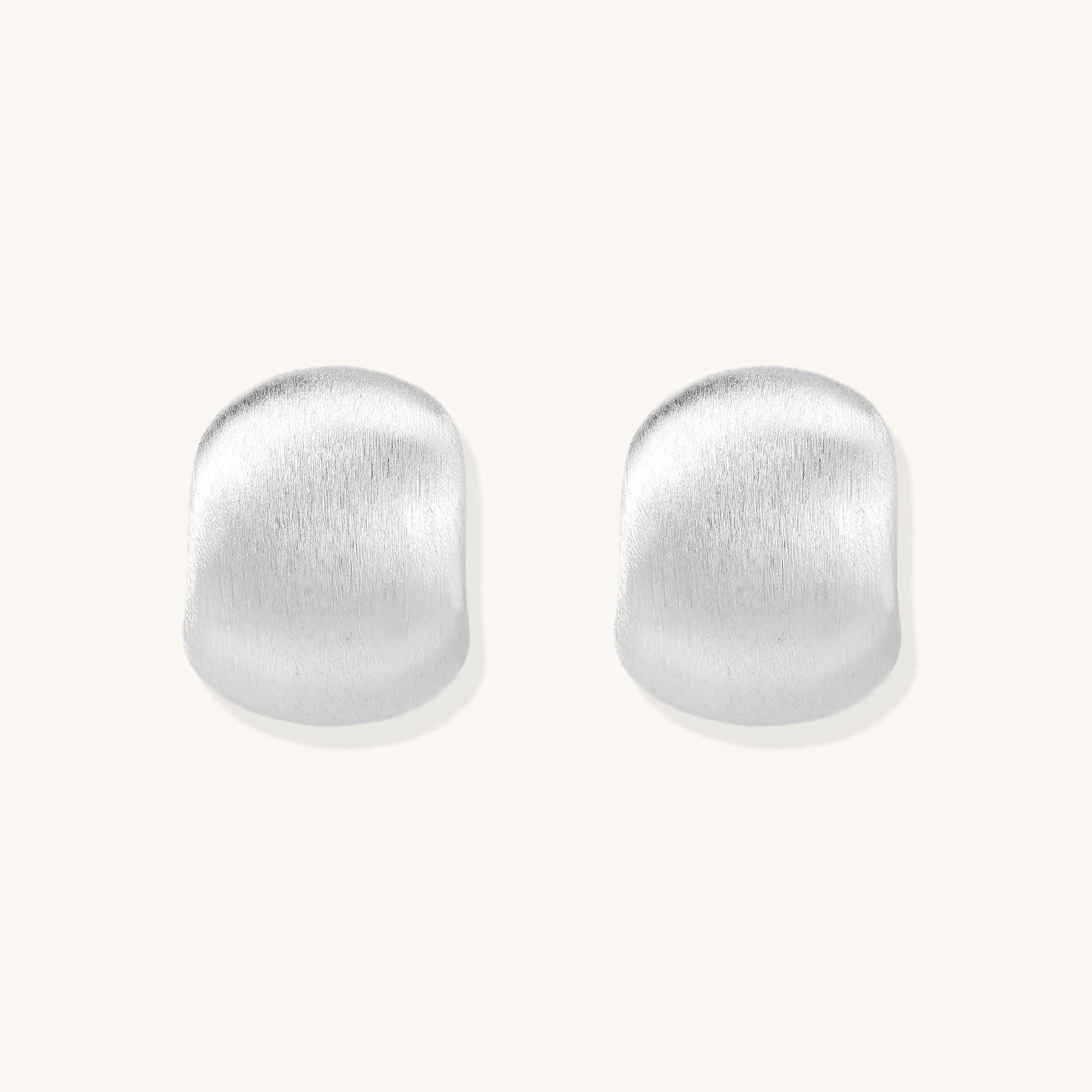 Close-up of chunky sterling silver huggie hoops with brushed matte finish against cream background.