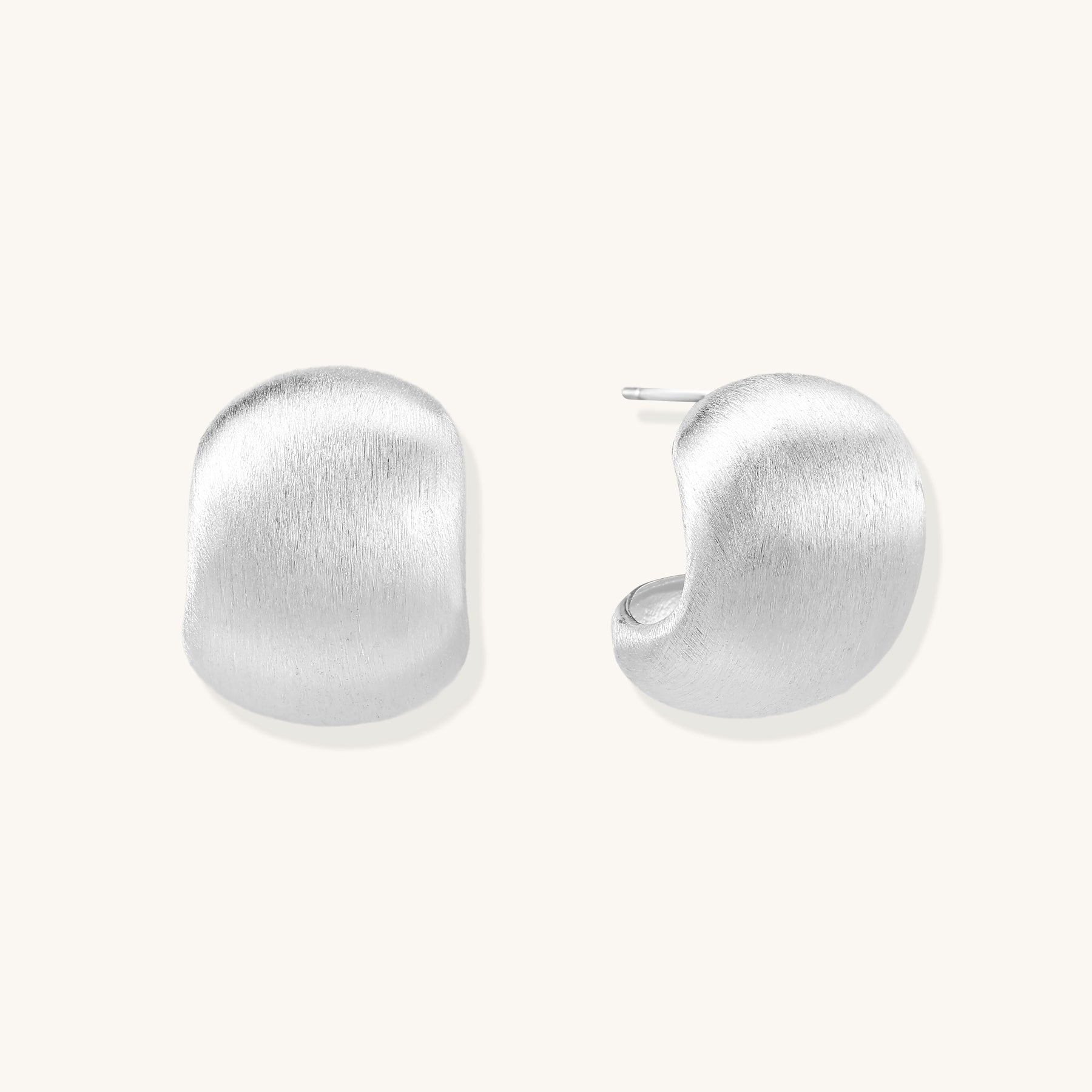 Close-up of chunky sterling silver huggie hoops with brushed matte finish against cream background.