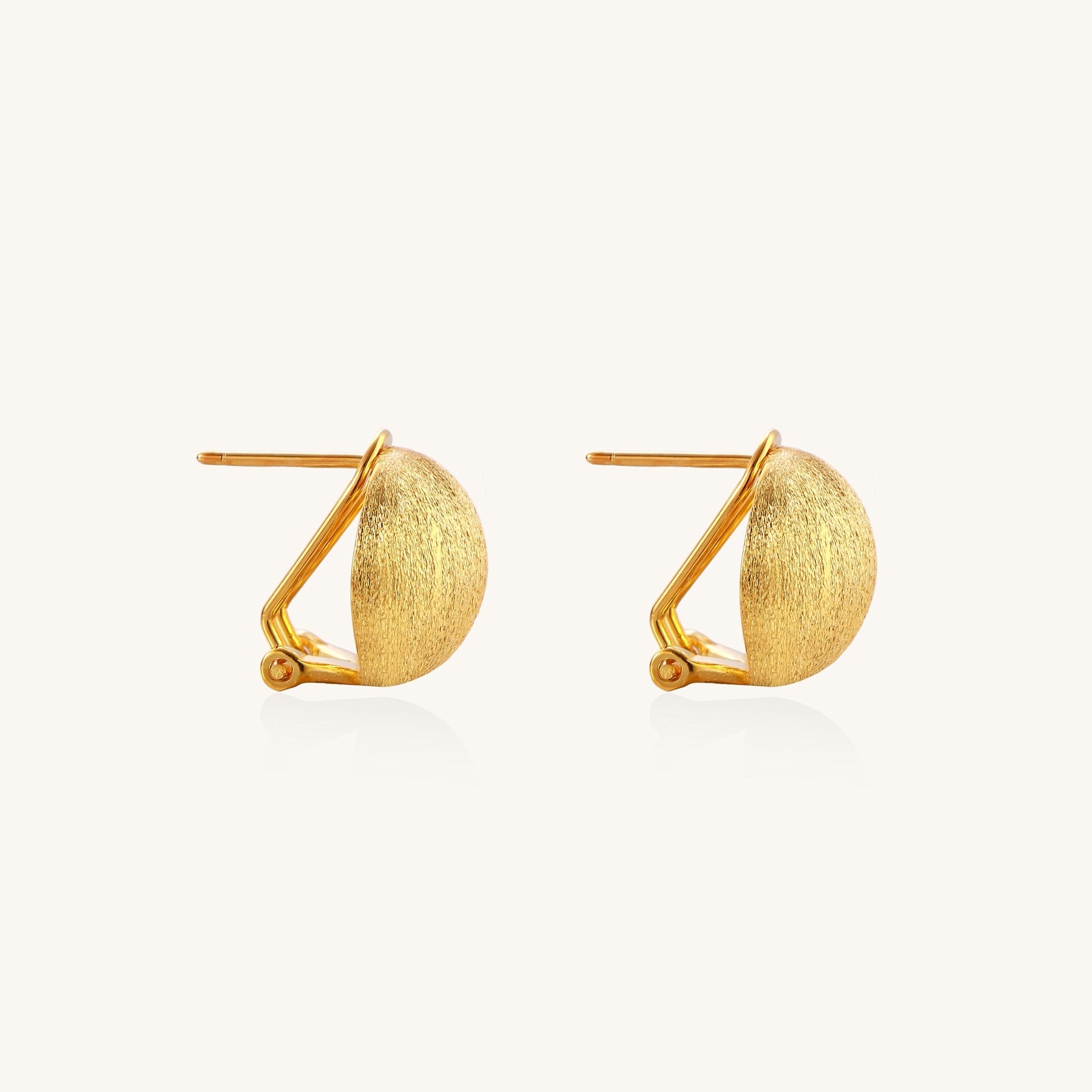 Close-up of textured gold-plated sterling silver dome clip-on earrings with brushed finish on white background.