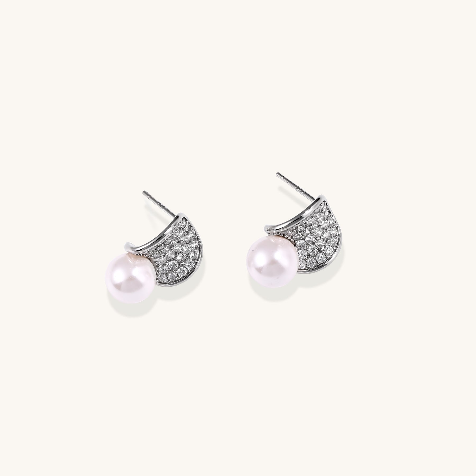 Elegant gold-plated curved earrings with diamond pavé crescents and suspended freshwater pearls on neutral background.