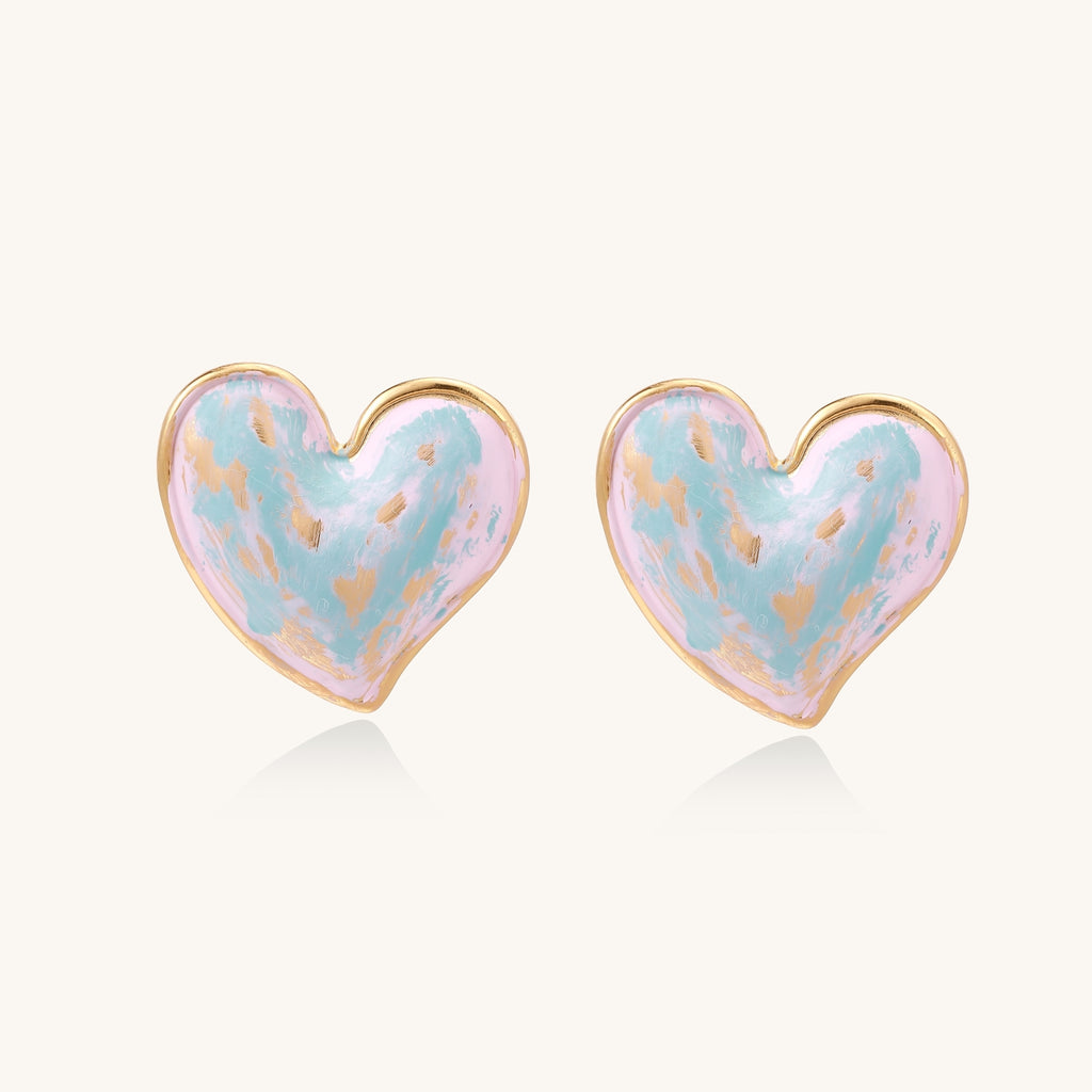 Heart-shaped stud earrings with iridescent blue-pink enamel finish and gold-plated brass frames against cream background
