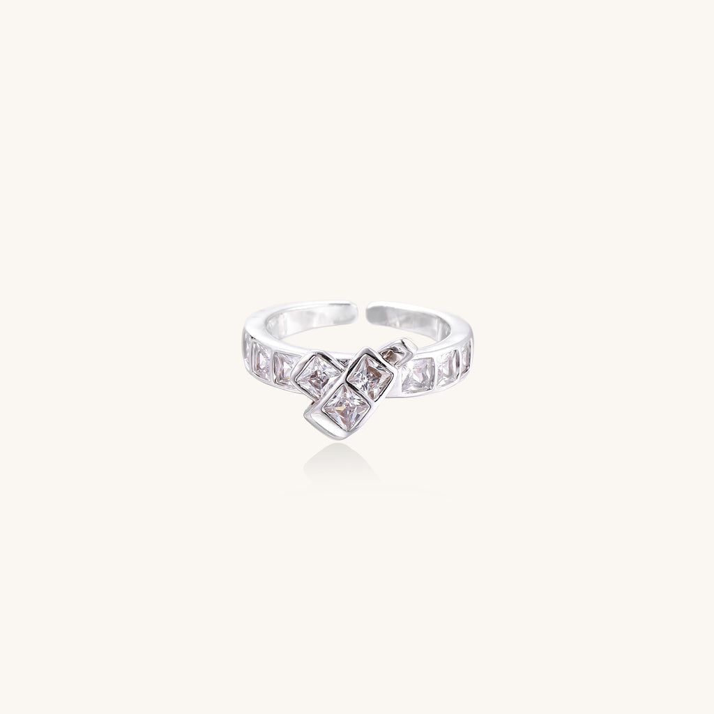 Close-up of geometric gold-plated brass ring with square-cut zirconia stones in architectural tiered design on white background.