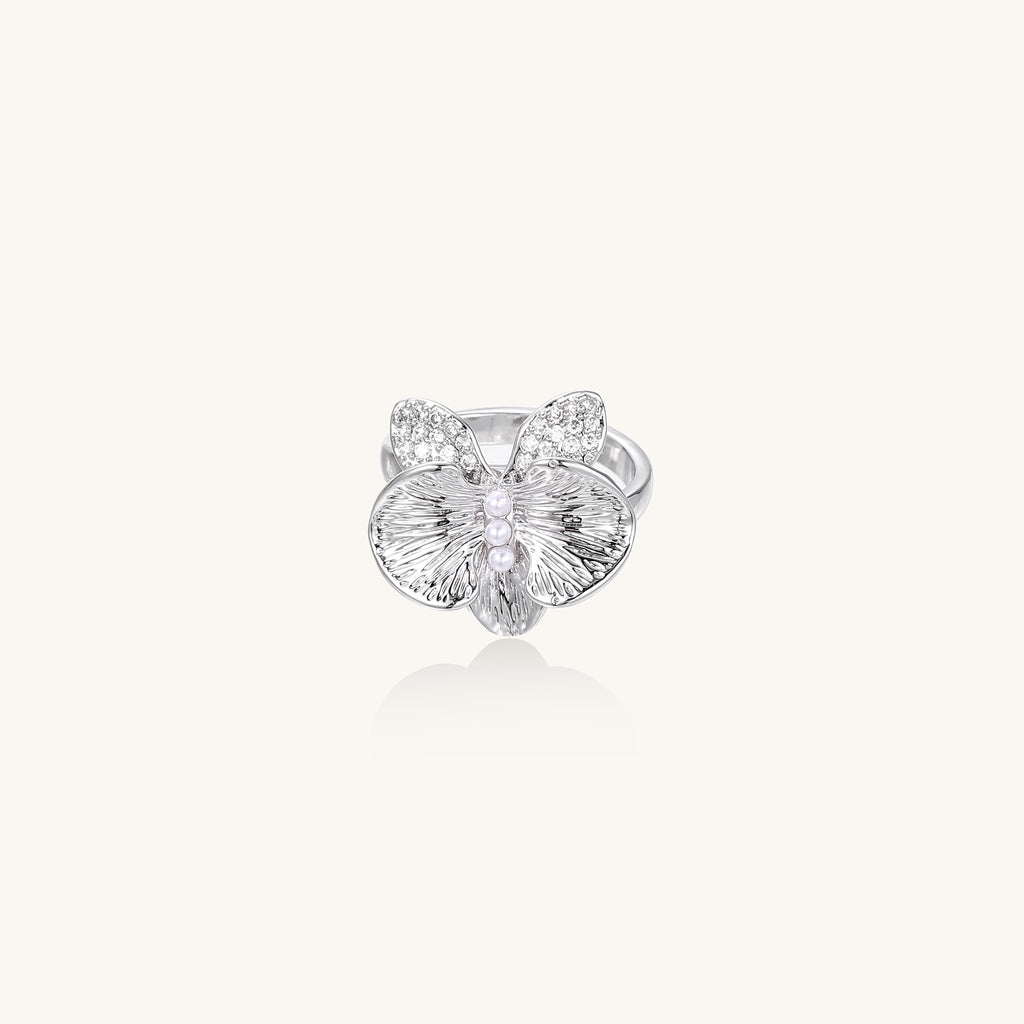 Gold-plated brass ring with textured orchid petals, zirconia stones, and center pearls on white background.