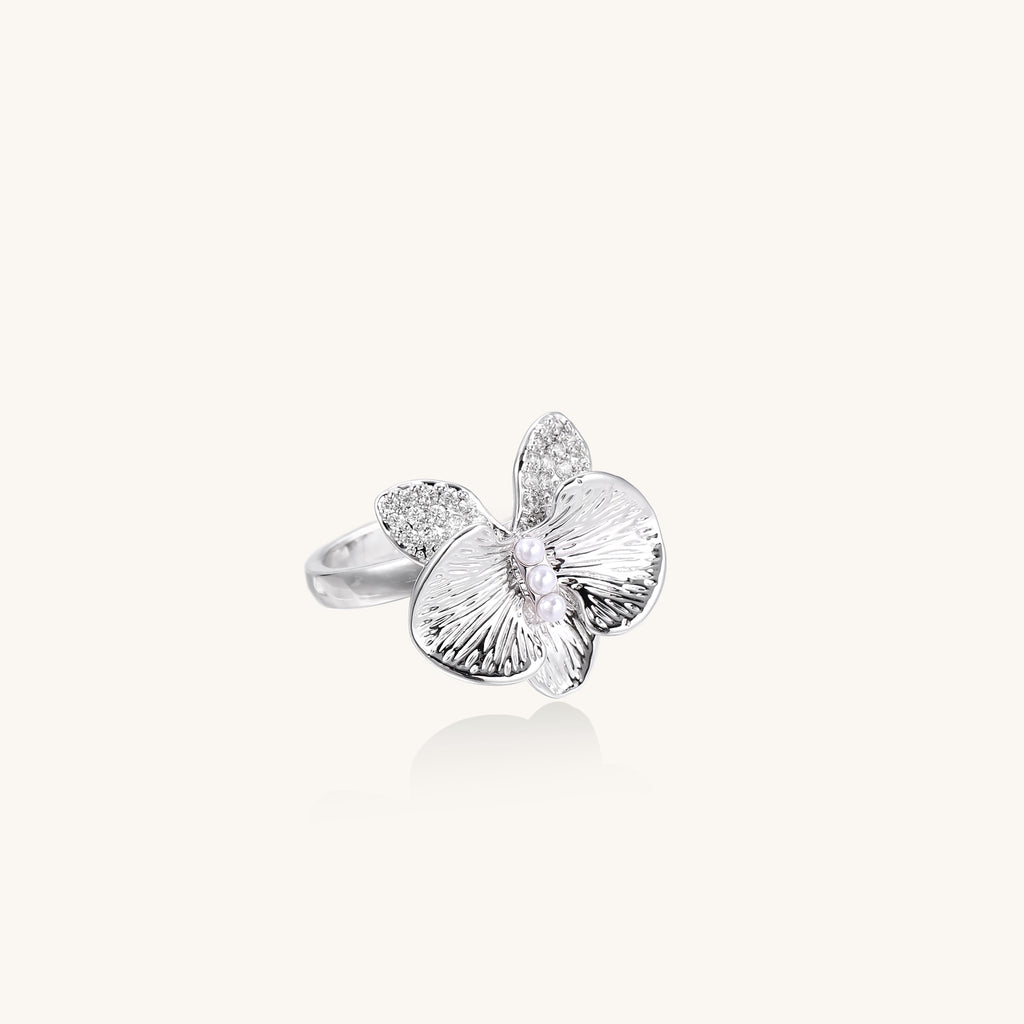Gold-plated brass ring with textured orchid petals, zirconia stones, and center pearls on white background.