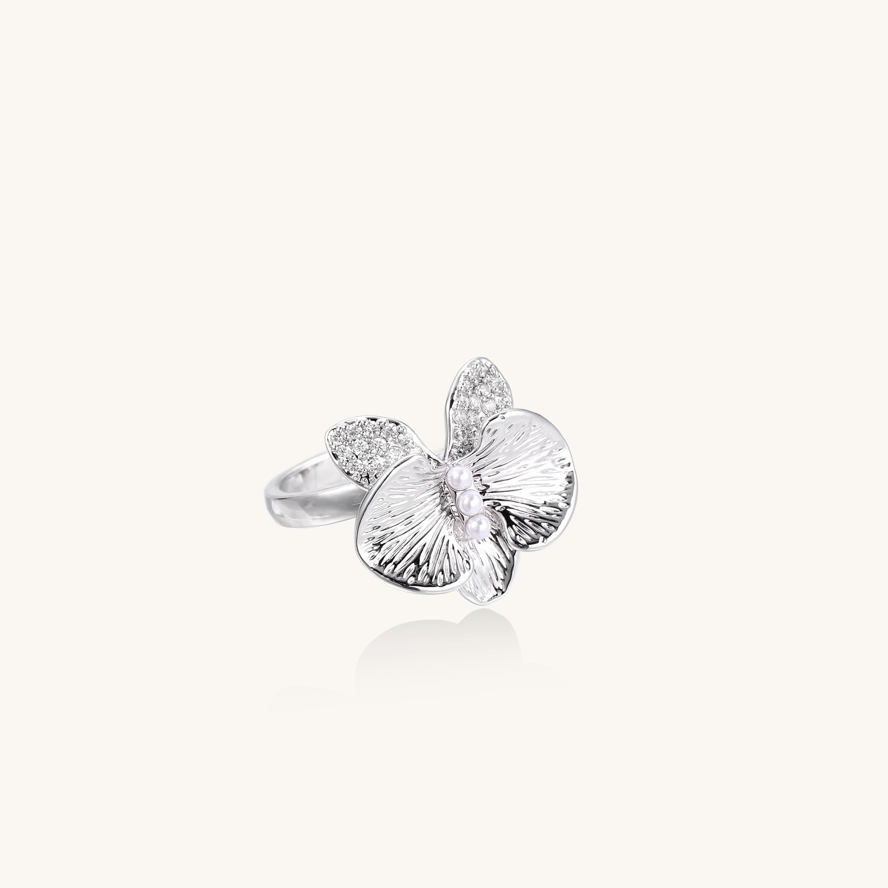 Gold-plated brass ring with textured orchid petals, zirconia stones, and center pearls on white background.