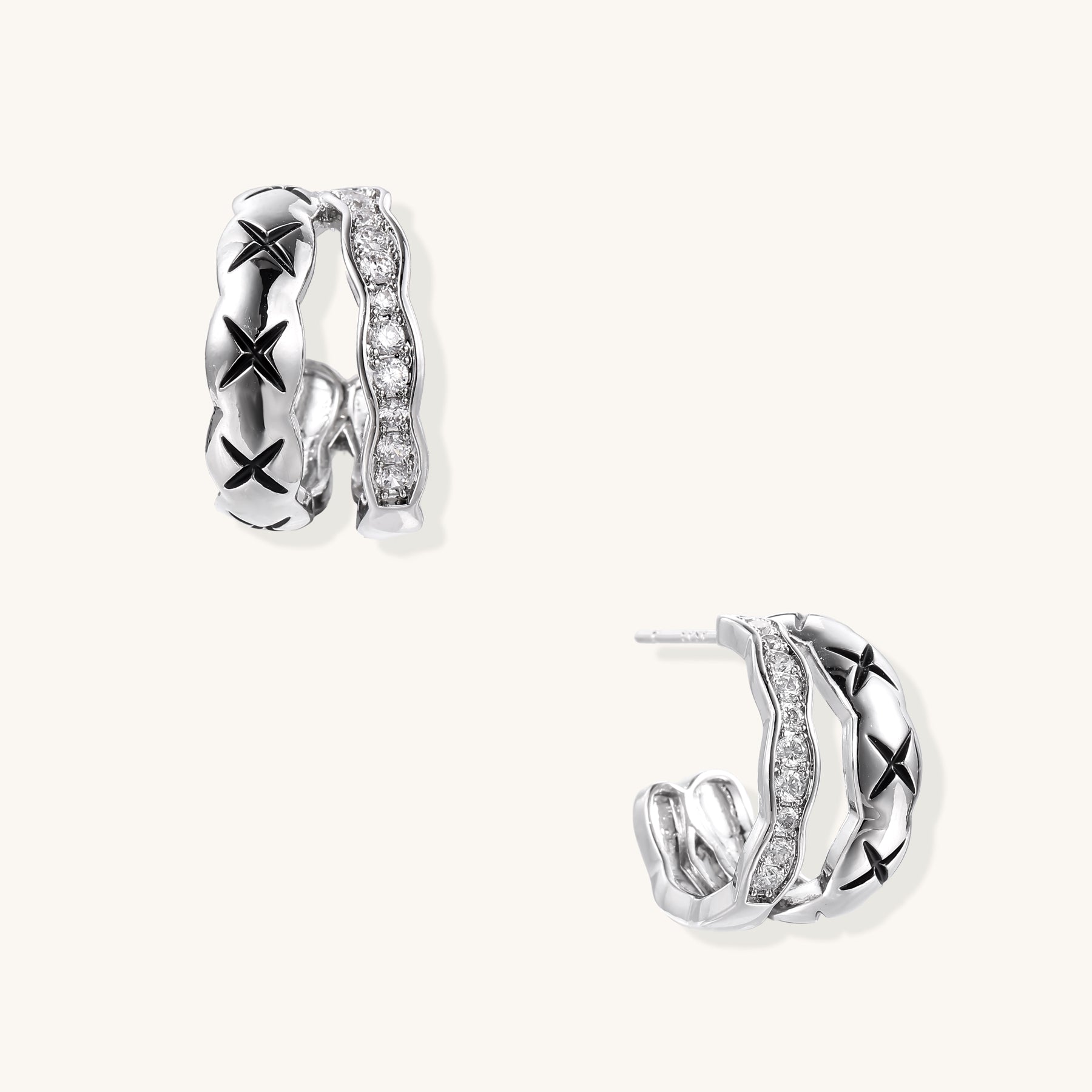 Close-up of gold-plated huggie earrings featuring X-pattern band and wavy zirconia-set band on white background.