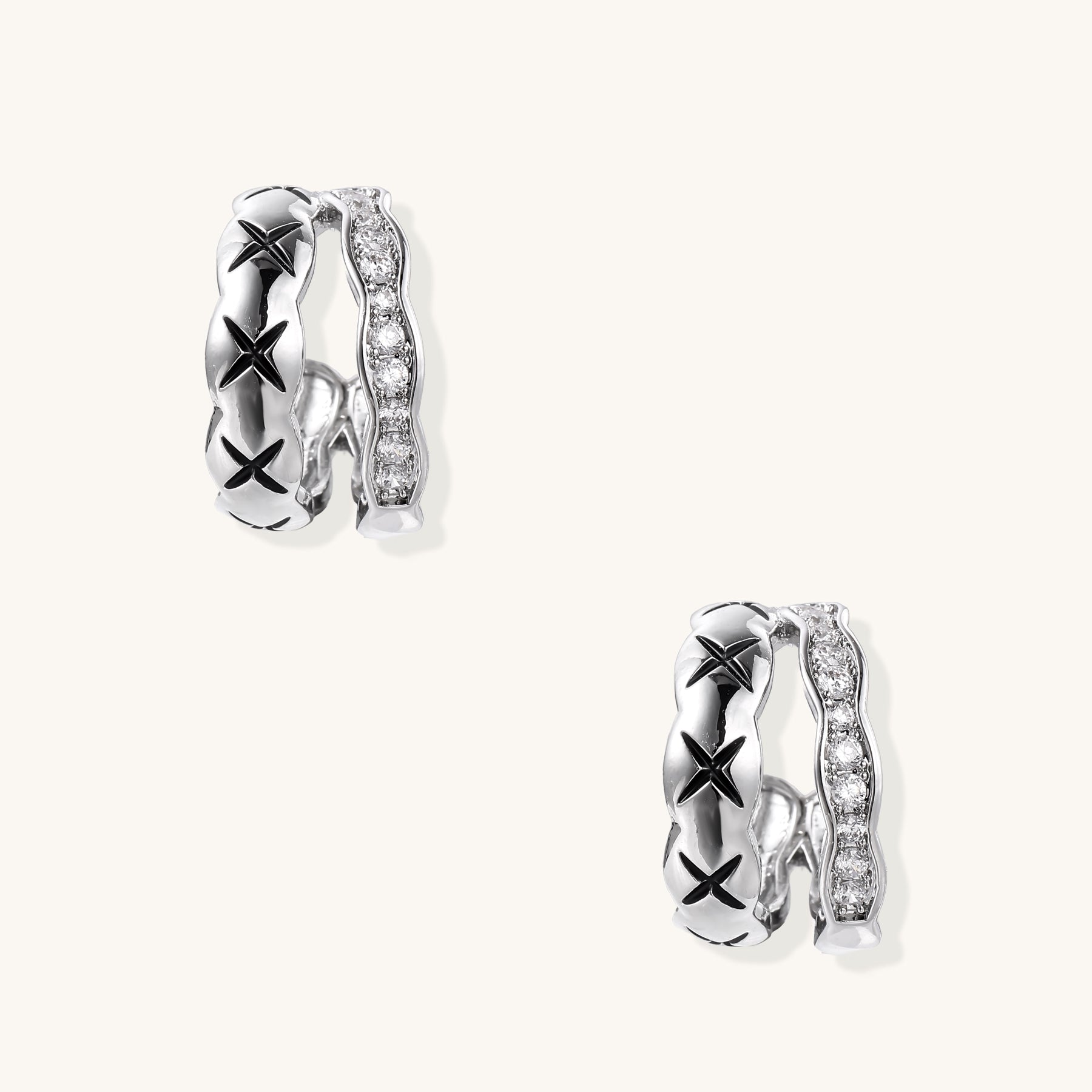 Close-up of gold-plated huggie earrings featuring X-pattern band and wavy zirconia-set band on white background.