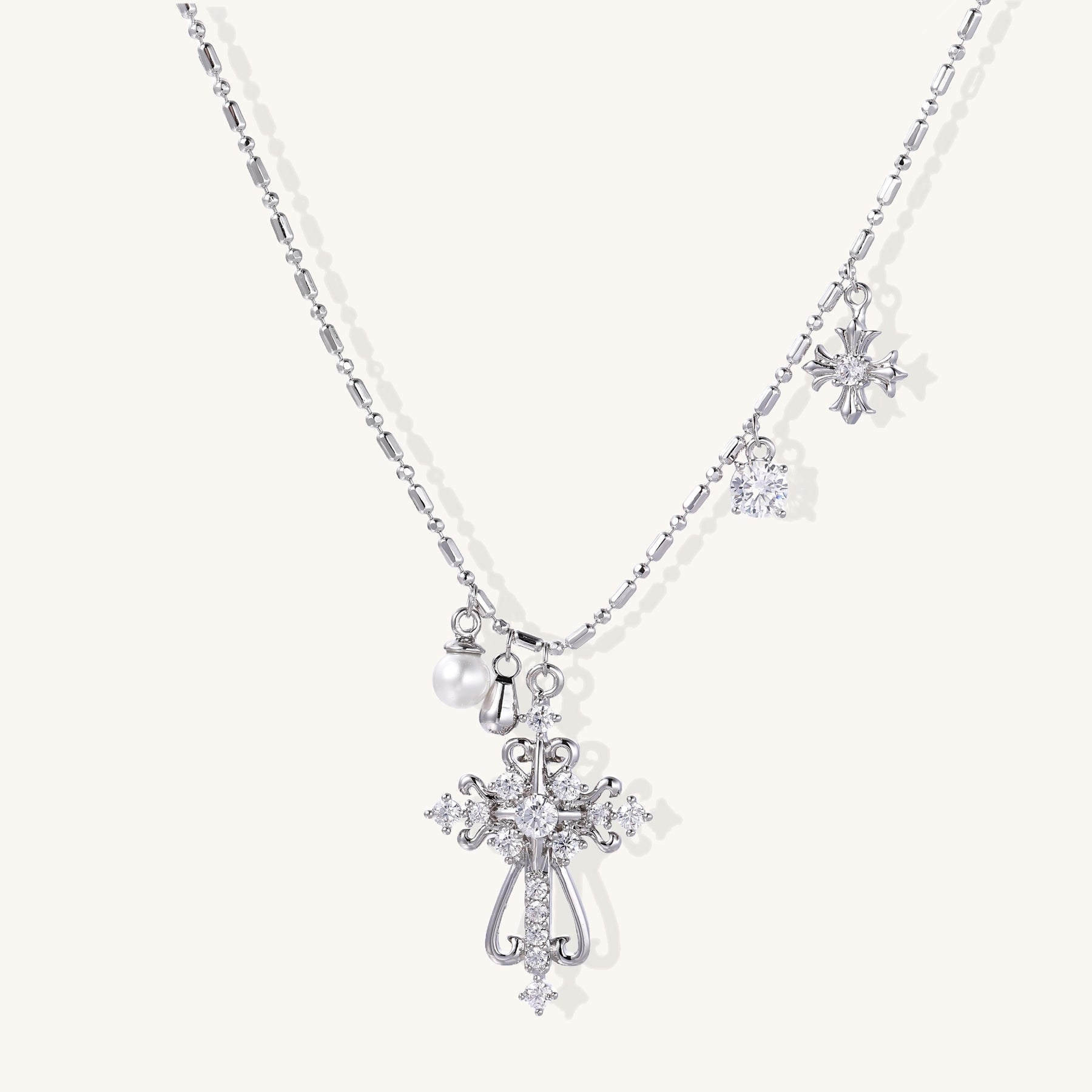 Layered gold-plated cross necklaces with baroque pearls and crystal embellishments on white background
