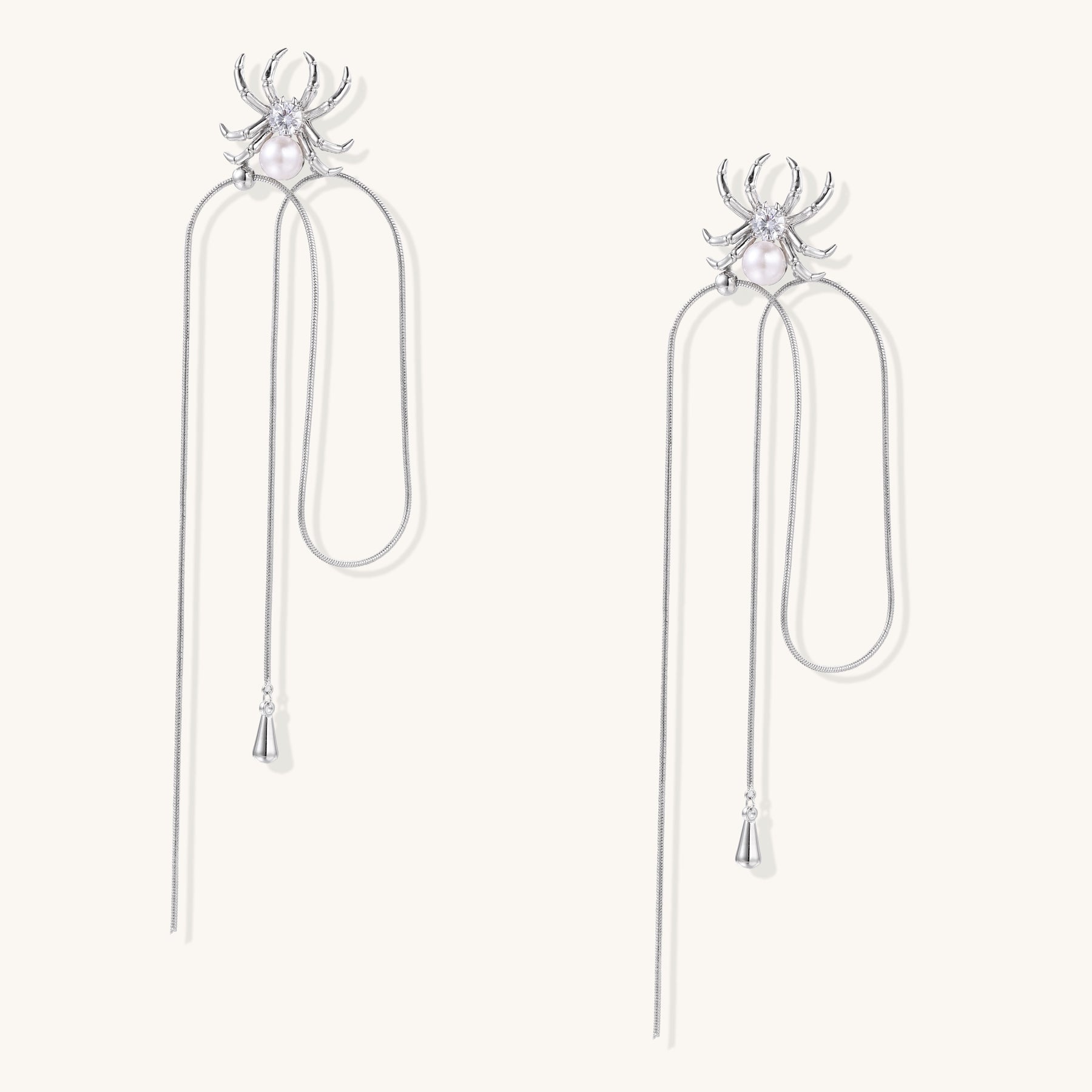 Two elegant gold-plated spider drop earrings with white pearls and long chain details on white background.