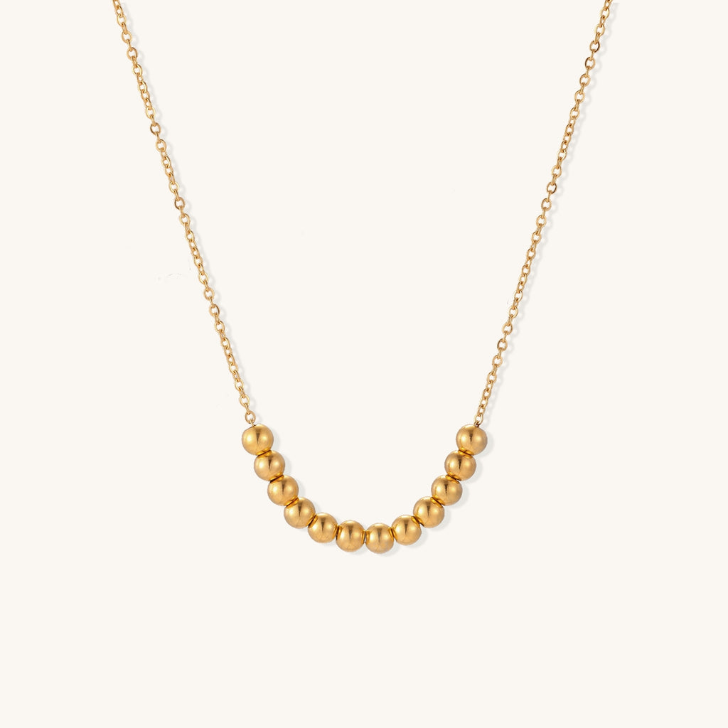 Delicate gold-plated chain necklace featuring clustered spherical beads arranged in elegant curve against white background.