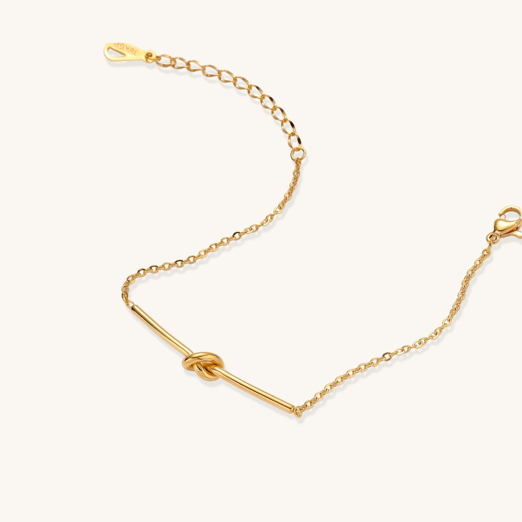 Delicate gold-plated chain bracelet with twisted knot bar detail and adjustable extender chain on white background.