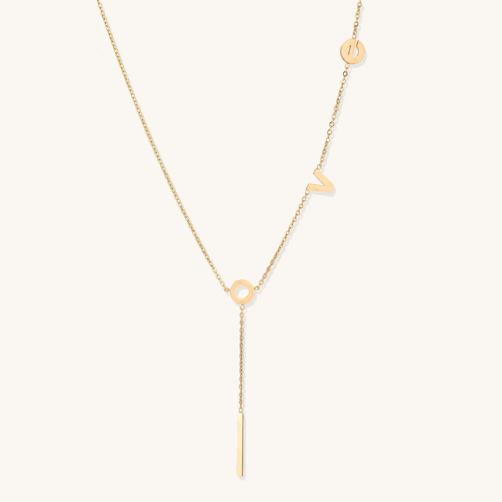 Gold-plated lariat necklace spelling LOVE with letter charms and vertical bar pendant on white background.