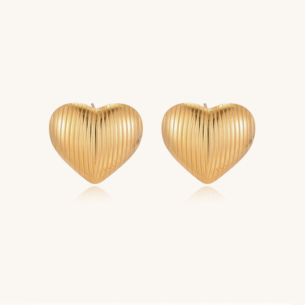 Close-up of ridged heart-shaped gold-plated stud earrings with textured surface pattern on cream background.