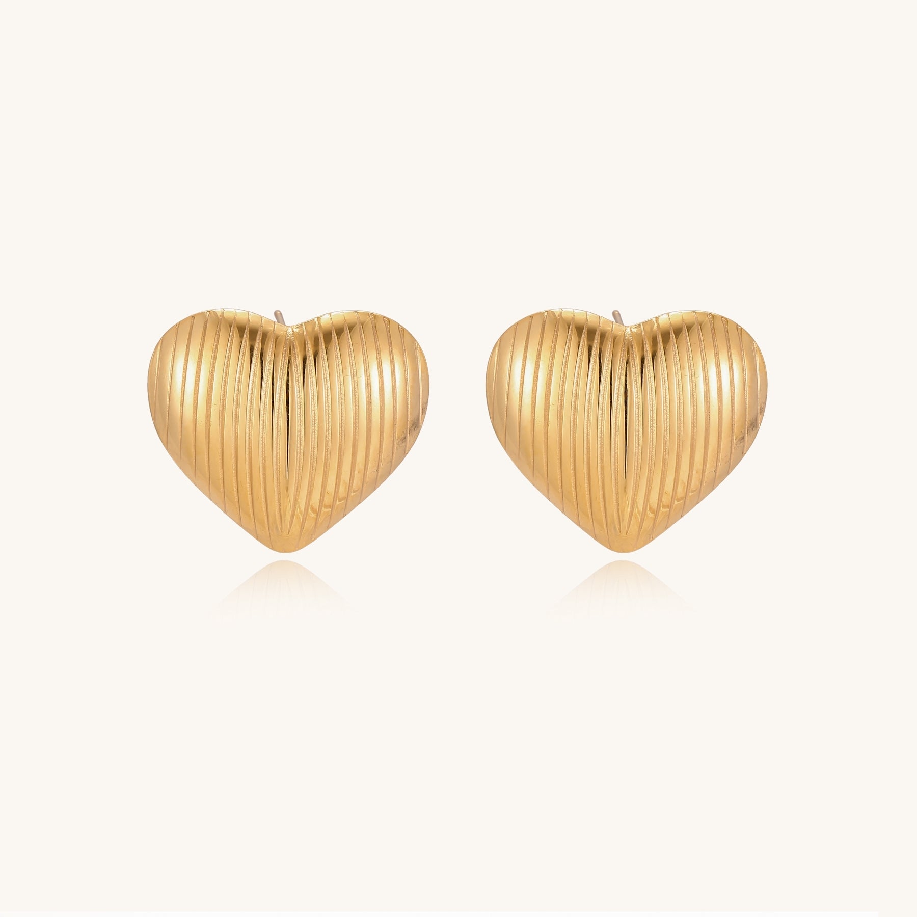 Close-up of ridged heart-shaped gold-plated stud earrings with textured surface pattern on cream background.