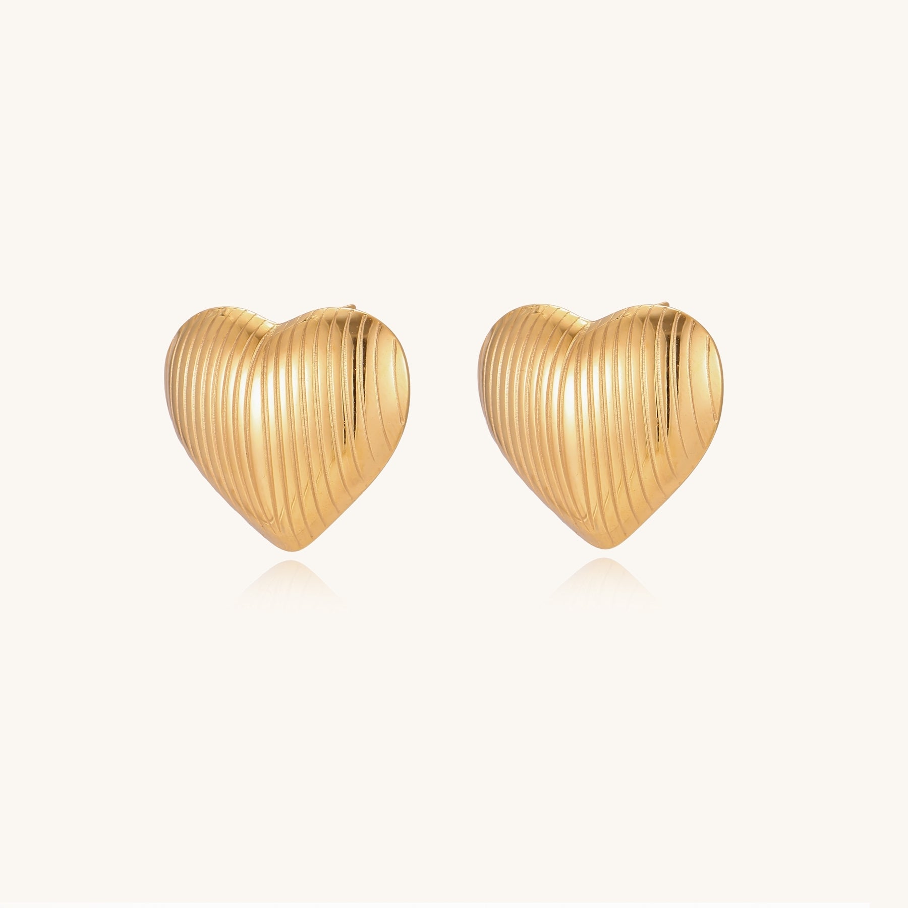 Close-up of ridged heart-shaped gold-plated stud earrings with textured surface pattern on cream background.