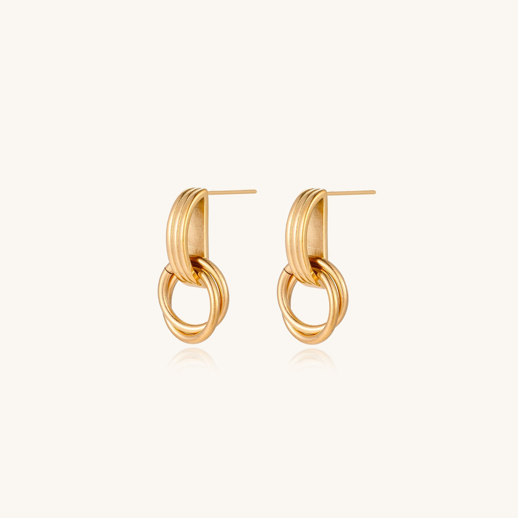 Geometric gold earrings with ribbed linear top section and circular drop elements on white background.