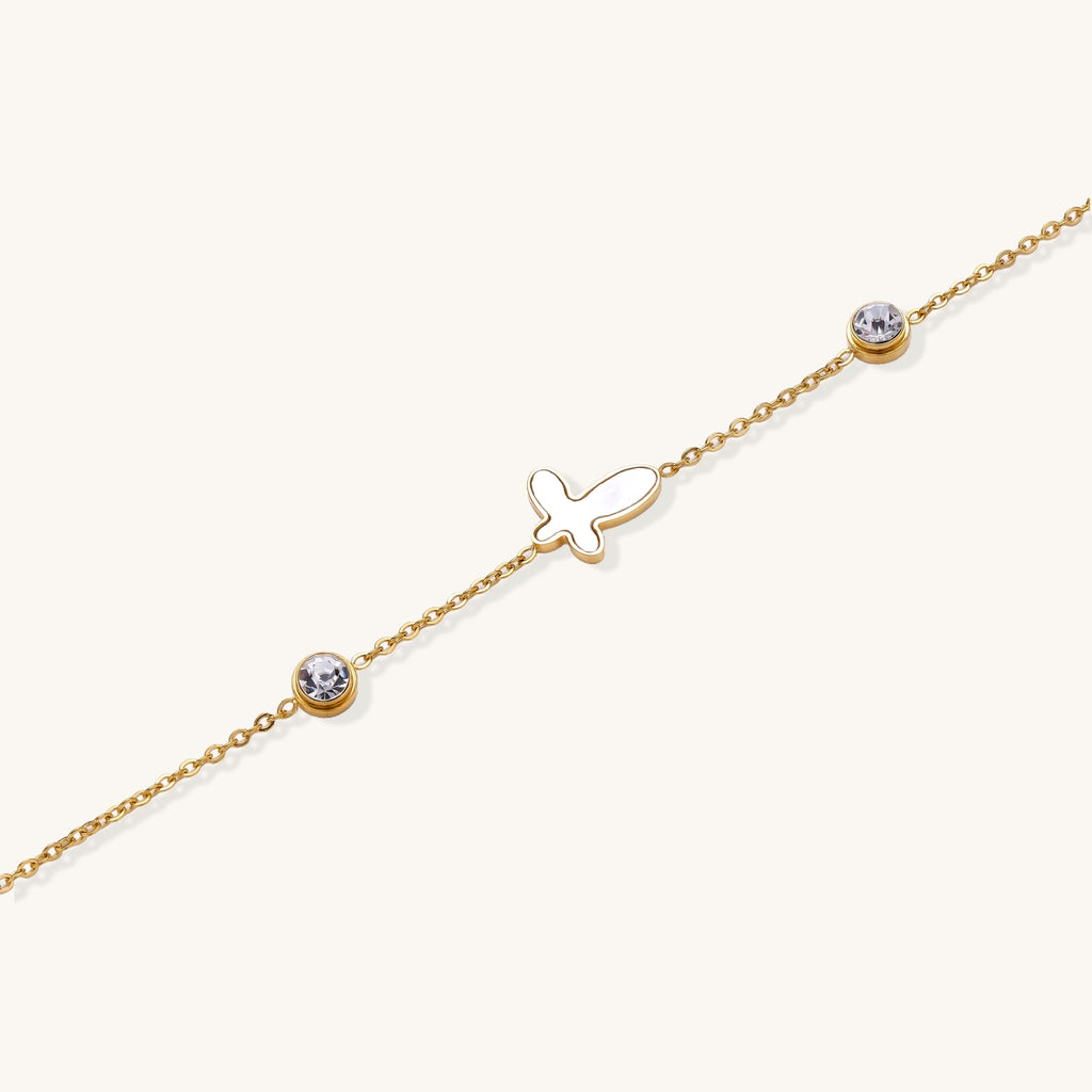 Delicate gold-plated bracelet featuring white mother-of-pearl cross charm and crystal accents on white background.